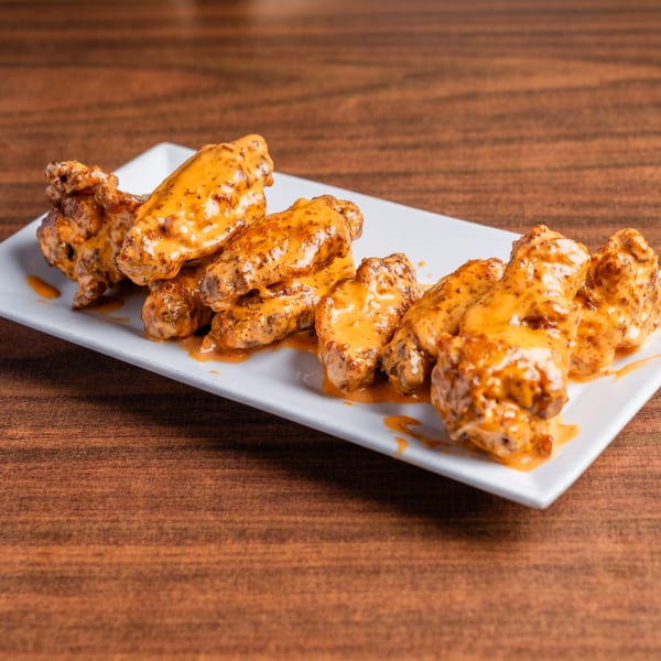 A white rectangular plate holds several chicken wings coated in a creamy orange sauce on a wooden table.