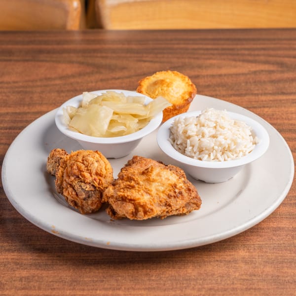 Fried chicken, rice, and cabbage served with a cornbread muffin on a white plate.