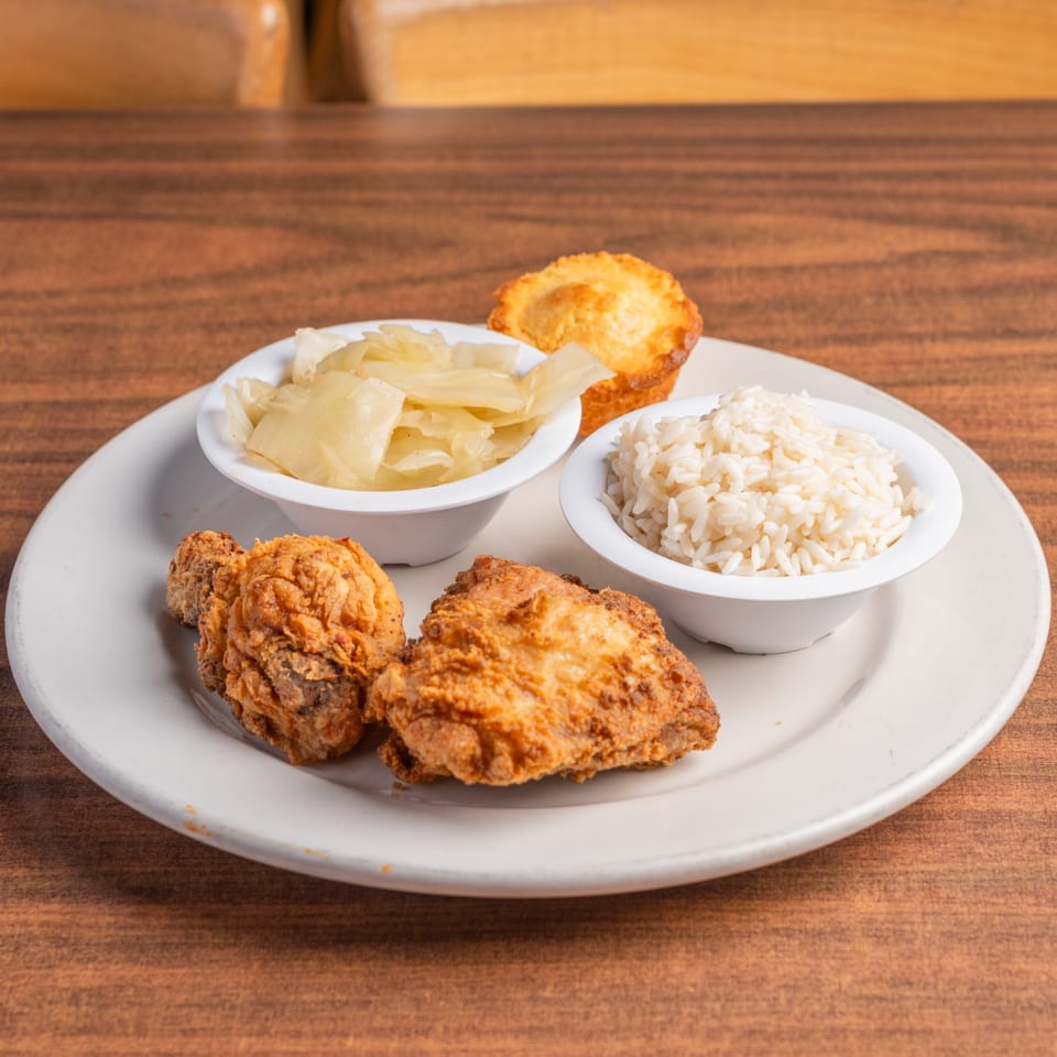 Fried chicken, rice, and cabbage served with a cornbread muffin on a white plate.