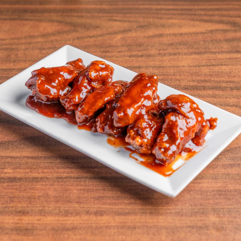 DeAngelo's Neapolitan Italian Eatery's chicken wings coated in a rich, glossy red sauce on a white rectangular plate.