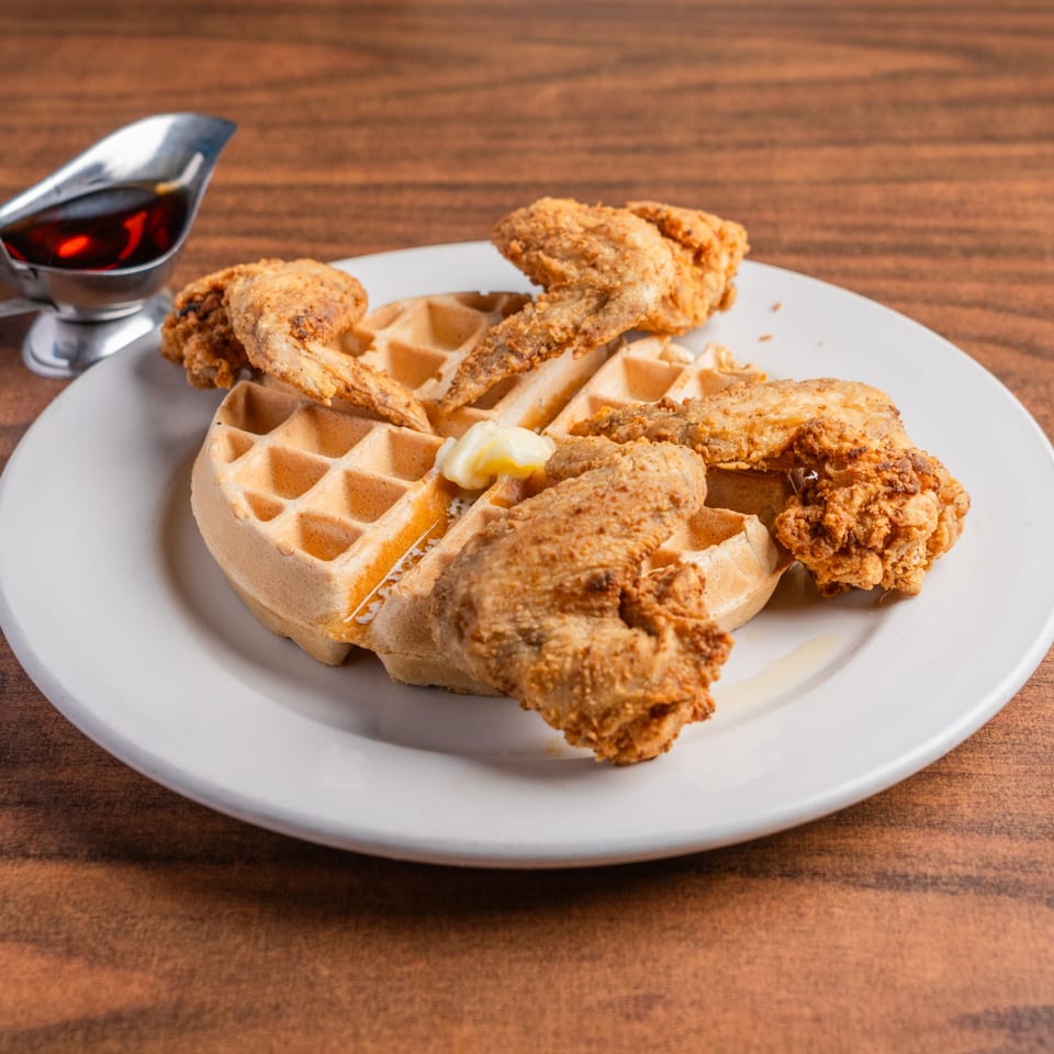Crispy fried chicken wings and a waffle with butter and syrup on a white plate.
