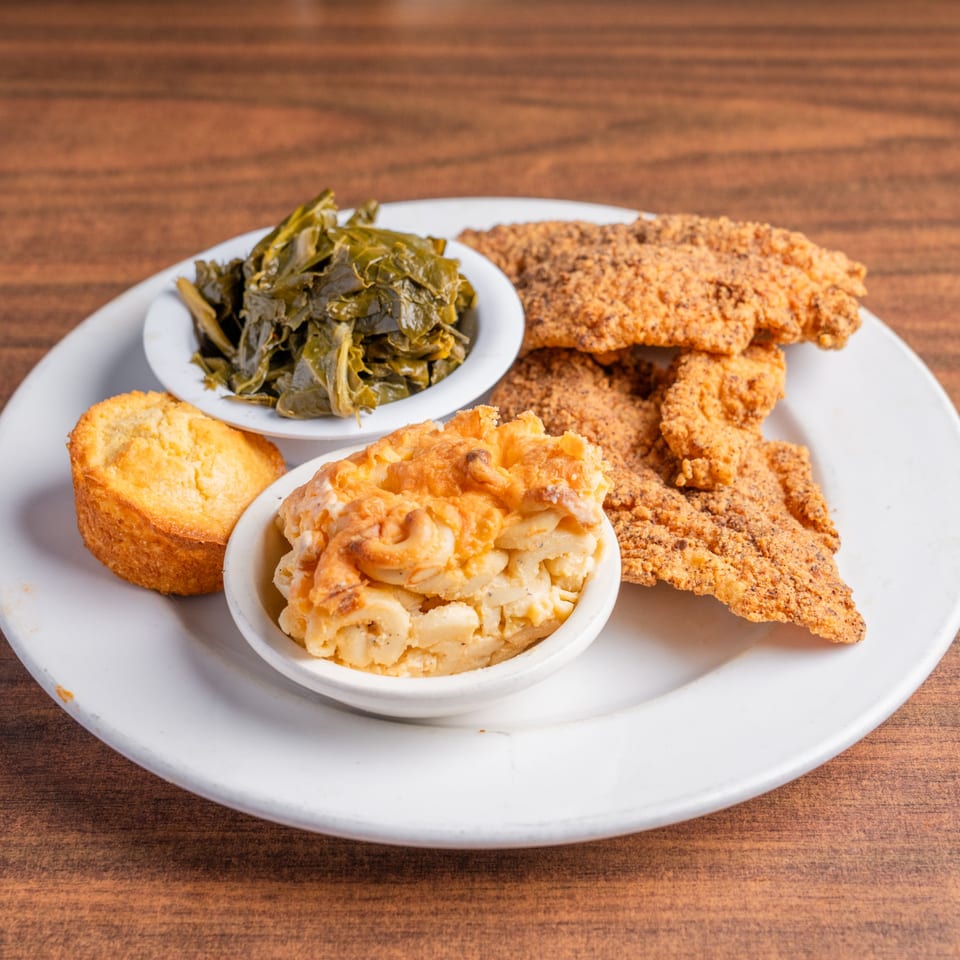 Fried fish fillets, collard greens, macaroni and cheese, and cornbread on a white plate.
