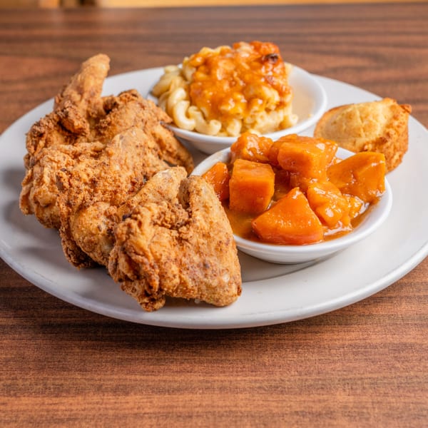 Fried chicken, macaroni and cheese, candied yams, and cornbread on a white plate.