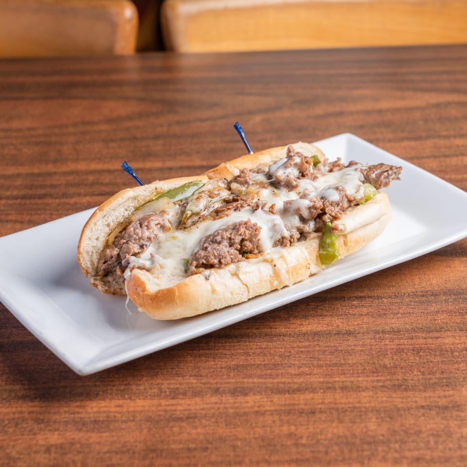 A DeAngelo's Neapolitan Italian Eatery cheesesteak sandwich with melted cheese, peppers, and onions on a white plate.